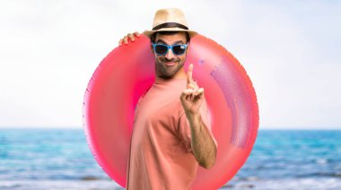 Onun yaz tatili gösteren ve plajda en iyi işareti bir parmak kaldırma üzerinde şapka ve güneş gözlüğü ile adam