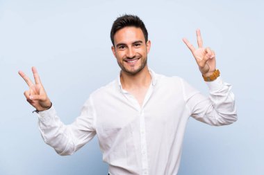 Her iki eliyle zafer işareti gösteren izole mavi arka planda yakışıklı genç adam
