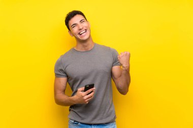 Zafer pozisyonunda telefon ile izole sarı duvar üzerinde Yakışıklı adam