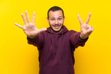 Sarı duvar üzerinde Sweatshirt olan Kolombiyalı adam yedi parmaklar ile sayma