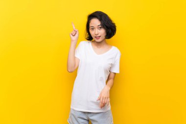Asyalı Genç kadın üzerinde izole sarı duvar bir parmak kaldırırken çözüm anlar niyetine