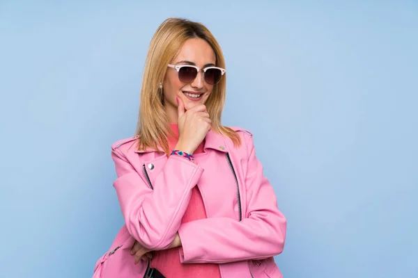 Молода Блондинка Рожевою Курткою Над Ізольованим Синім Тлом Окулярами Посмішкою — стокове фото