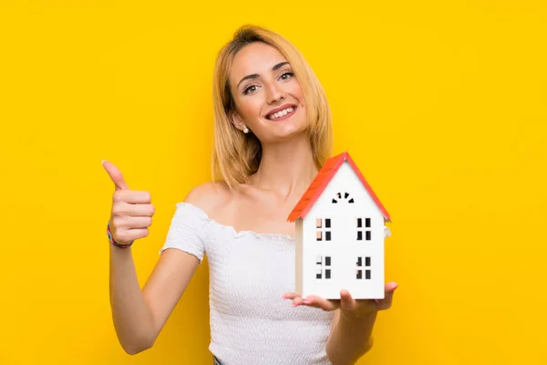 Jonge Blonde Vrouw Geïsoleerde Gele Muur Holding Een Huisje — Stockfoto