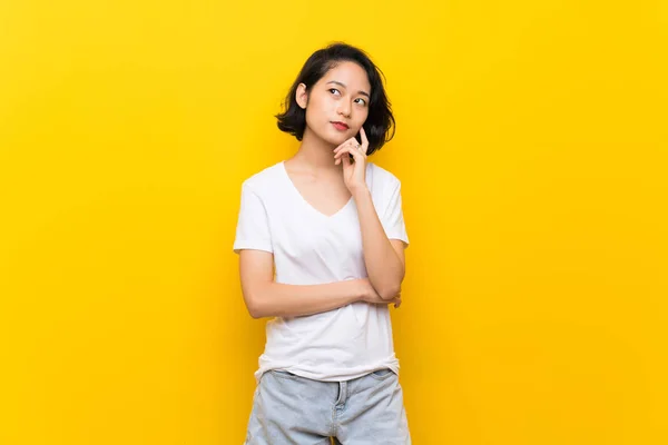 Азіатські Молода Жінка Над Ізольованою Жовта Стіна Думає Ідея Шукаючи — стокове фото