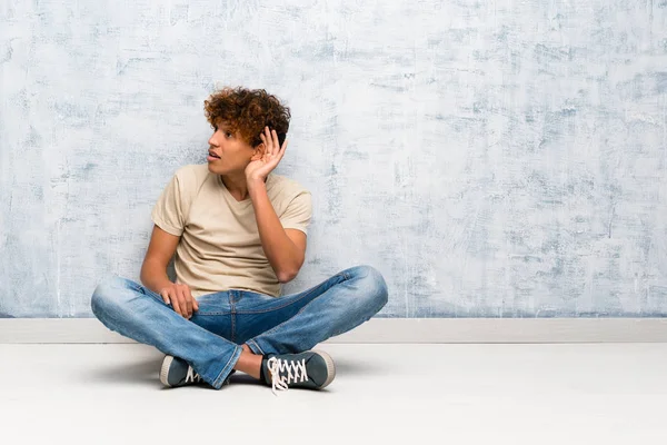 Νεαρός Αφροαμερικάνος Κάθεται Στο Πάτωμα Ακούγοντας Κάτι Βάζοντας Χέρι Του — Φωτογραφία Αρχείου