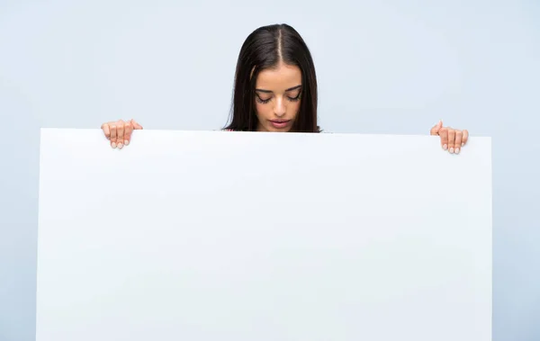 年轻女子在孤立的蓝色墙壁上拿着一个空的白色标语牌插入一个概念 — 图库照片