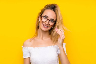 Gözlüklü izole sarı duvar üzerinde genç sarışın kadın