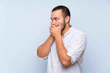 İzole mavi duvar ağız kapsayan üzerinde Kolombiyalı adam ve yan bakıyor