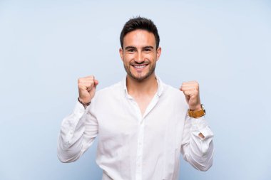 Kazanan pozisyonda zafer kutluyor izole mavi arka plan üzerinde yakışıklı genç adam