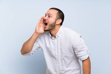 İzole mavi duvar üzerinde Kolombiyalı adam ağız geniş lateral açık bağırarak