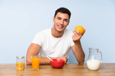 Kahvaltı ve turuncu tutan yakışıklı adam