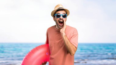 Onun yaz tatili üzerinde şapka ve güneş gözlüğü ile adam ağız geniş açık ve plajda bir şey duyurarak bağırıyor