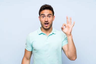 İzole arka plan üzerinde yakışıklı genç adam şaşırttı ve ok işareti gösteren