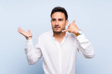 İzole mavi arka plan üzerinde yakışıklı genç adam telefon jest yapma ve şüphe