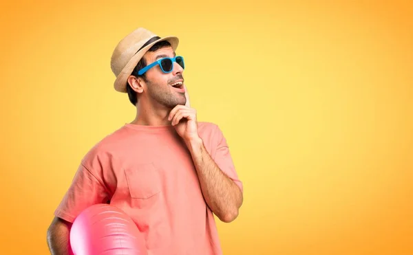 彼の夏休みに帽子とサングラスを持つ男は オレンジ色の背景を見上げながら立ってアイデアを考えています — ストック写真