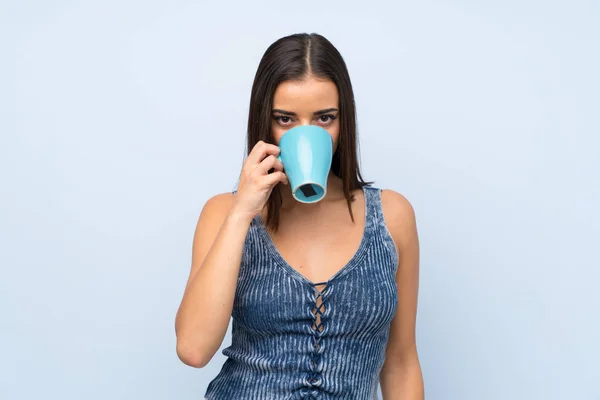 Молода Жінка Над Ізольованою Синьою Стіною Тримає Гарячу Чашку Кави — стокове фото