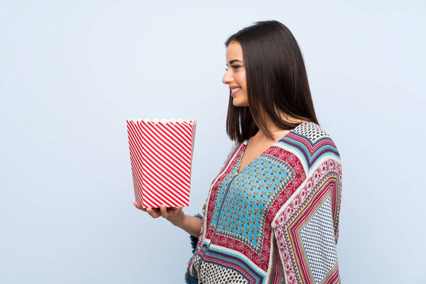 Young woman over isolated blue wall holding a bowl of popcorns