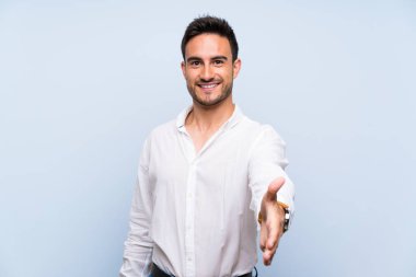 İyi bir anlaşma kapanış için izole mavi arka plan sallayarak eller üzerinde yakışıklı genç adam