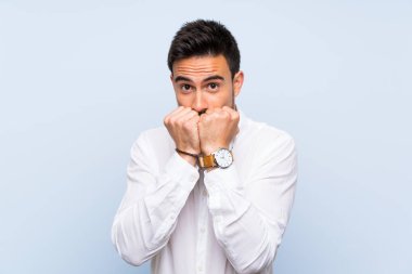 İzole mavi arka plan üzerinde yakışıklı genç adam sinir ve ağız eller koyarak korkuyor