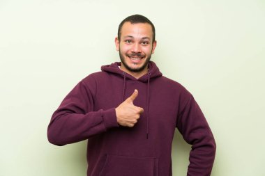 Bir başparmak yukarı jest vererek yeşil duvara Sweatshirt ile Kolombiyalı adam