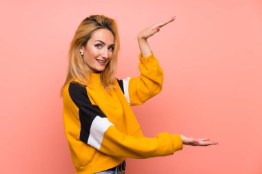 İzole edilmiş pembe arka planı olan genç sarışın kadın ilan vermek için kopyalama alanı tutuyor.