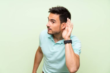 İzole arka plan üzerinde yakışıklı genç adam kulak el koyarak bir şey dinliyor