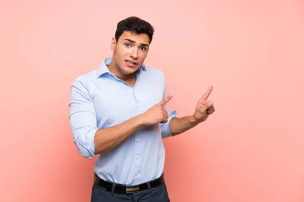 Handsome man over pink background frightened and pointing to the side