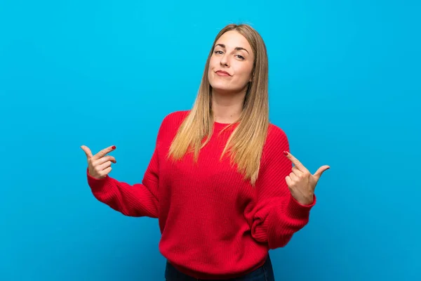 Woman with red sweater over blue wall proud and self-satisfied