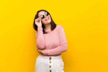 Young Mexican woman over isolated yellow background with glasses and happy