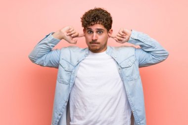 Elleriyle her iki kulağı kapsayan pembe duvar üzerinde Sarışın adam