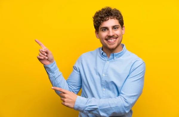 Biondo Uomo Oltre Isolato Muro Giallo Puntando Dito Verso Lato — Foto Stock