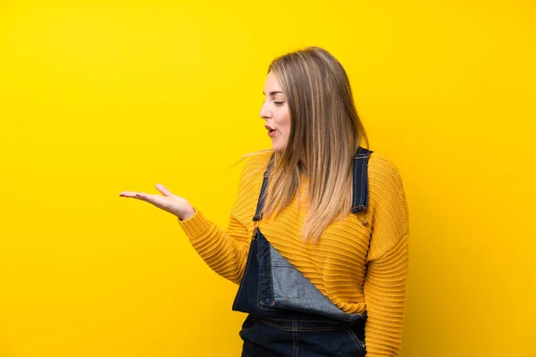 Vrouw Met Overalls Geïsoleerde Gele Muur Met Kopieerruimte Denkbeeldig Palm — Stockfoto
