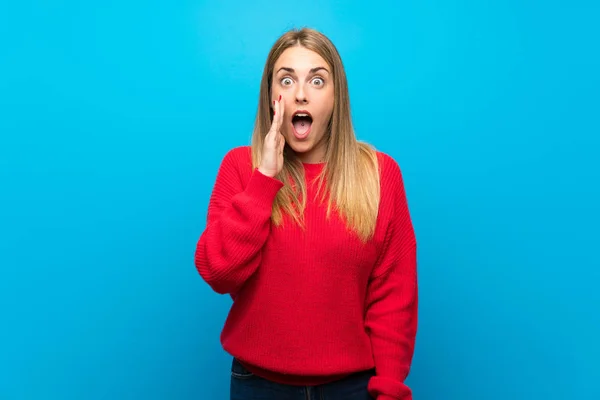 驚きとショックを受けた顔の表情で青い壁に赤いセーターを持った女性 — ストック写真