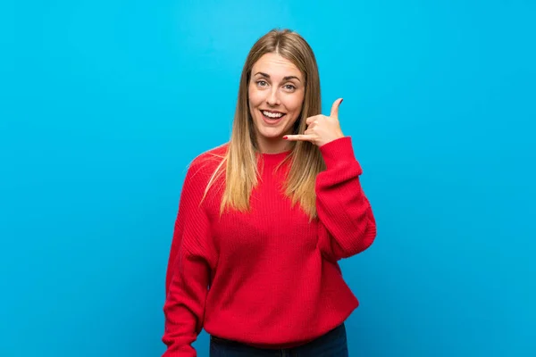 Woman with red sweater over blue wall making phone gesture. Call me back sign