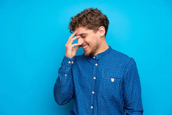 Blonde man over isolated blue wall laughing