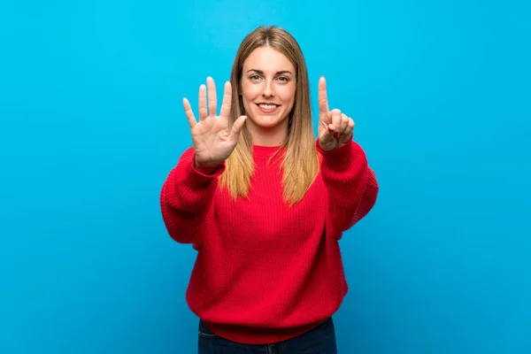 Woman with red sweater over blue wall counting six with fingers