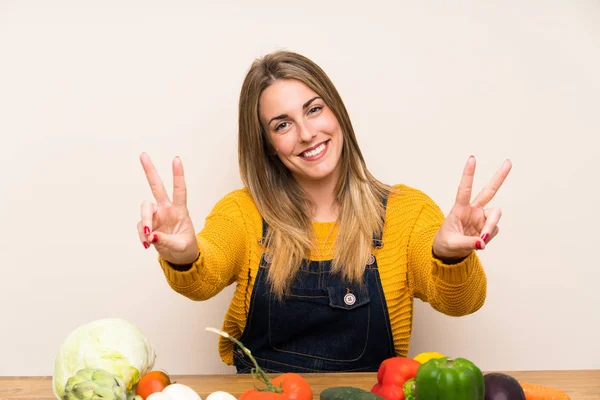 Woman with lots of vegetables smiling and showing victory sign