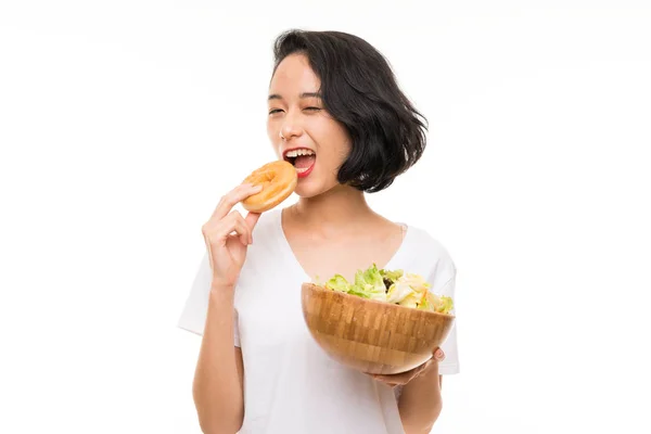 Asiática joven mujer sobre aislado fondo con ensalada y donut — Foto de Stock