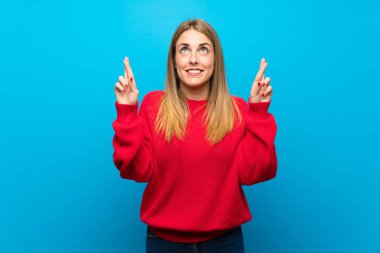 En iyi dilek ve geçiş parmak ile mavi duvarın üzerinden kırmızı kazaklı kadın