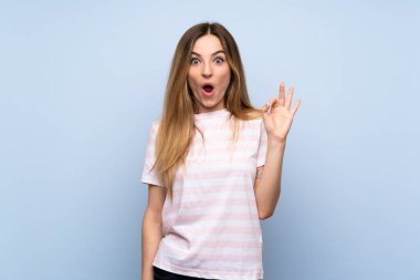 Izole mavi arka plan üzerinde genç kadın şaşırttı ve ok işareti gösteren