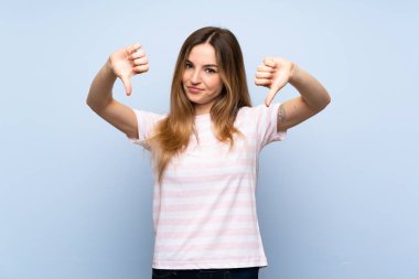 İzole edilmiş mavi arka planda genç bir kadın baş parmağını aşağı gösteriyor.