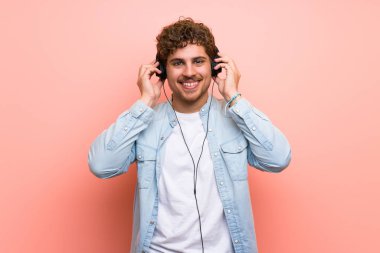 Sarışın adam pembe duvar üzerinde kulaklık ile müzik dinlerken
