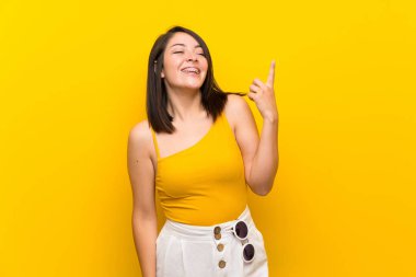 Young Mexican woman over isolated yellow background pointing up and surprised