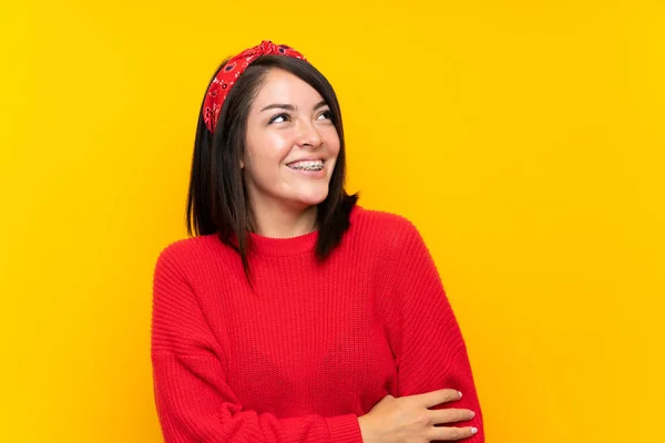 年轻的墨西哥女人与红色毛衣在黄墙上笑 — 图库照片