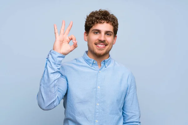 Blond Człowiek Nad Niebieską Ścianę Pokazując Znak Palcami — Zdjęcie stockowe