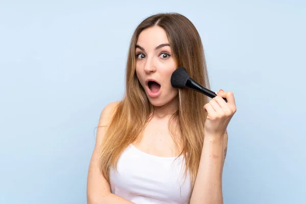 Jovem Mulher Sobre Fundo Azul Isolado Com Pincel Maquiagem — Fotografia de Stock