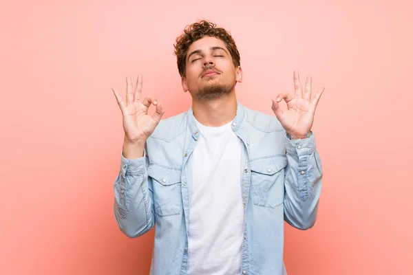 Blonde man over pink wall in zen pose