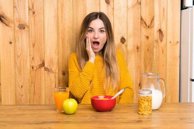 Genç bir kadın şaşırmış ve şok olmuş bir yüz ifadesiyle mutfakta kahvaltı yapıyor.