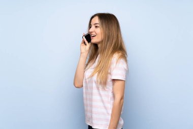 İzole edilmiş mavi arka planı olan genç bir kadın cep telefonuyla sohbet ediyor.