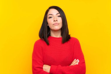 Young Mexican woman with red sweater over yellow wall keeping arms crossed